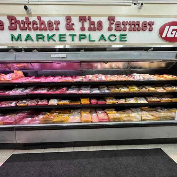 Rows of fresh-cut beef, pork and chicken under the Butcher & The Farmer Marketplace sign at Butcher & Farmer Market in Buckeye, AZ.