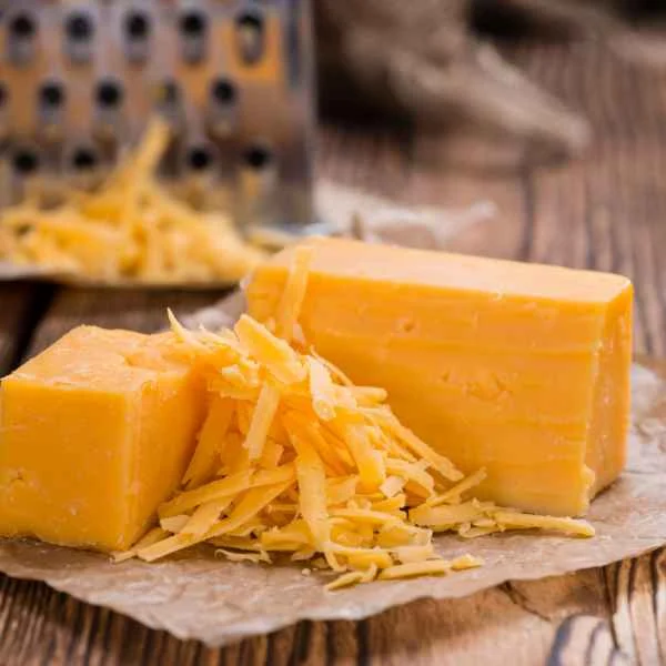 Blocks of cheddar cheese with freshly shredded cheese on a wooden board