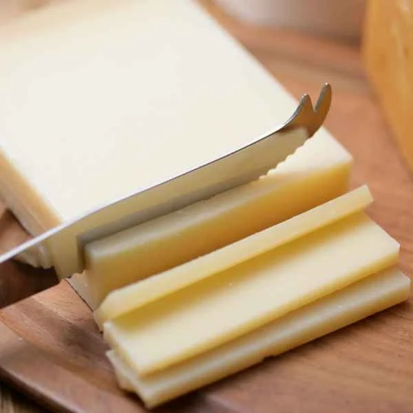 Knife slicing a block of white cheese on a wooden board