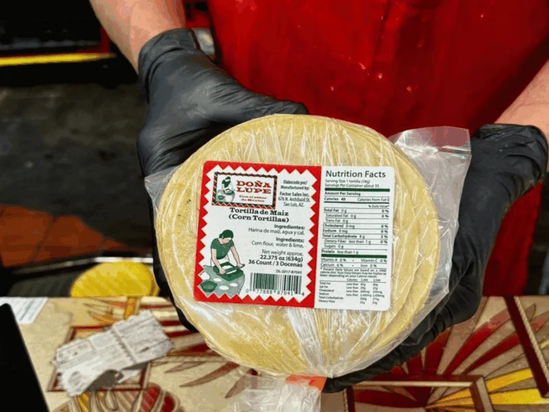 Team member holding a fresh package of Doña Lupe corn tortillas at Del Sol on 16th Street in Yuma, AZ