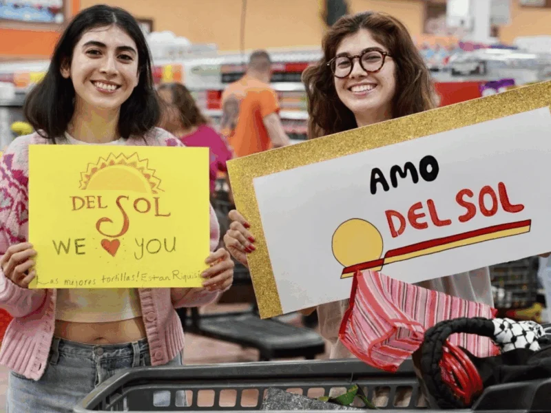 Smiling shoppers holding Amo Del Sol and Del Sol We Love You signs at Del Sol in the Yuma Foothills, AZ