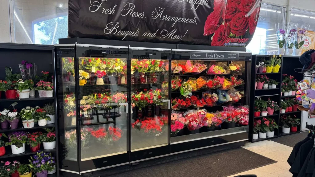 Floral cooler filled with roses, bouquets and potted plants under a Fresh Roses, Arrangements, Bouquets and More sign