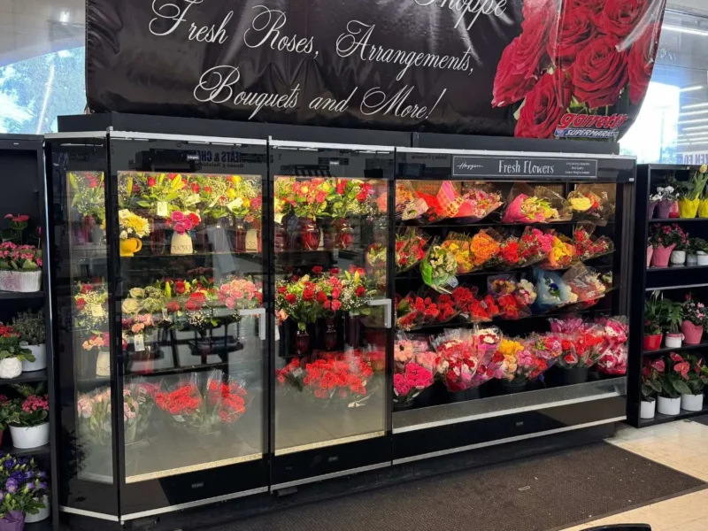 Floral cooler filled with roses, bouquets and potted plants under a Fresh Roses, Arrangements, Bouquets and More sign
