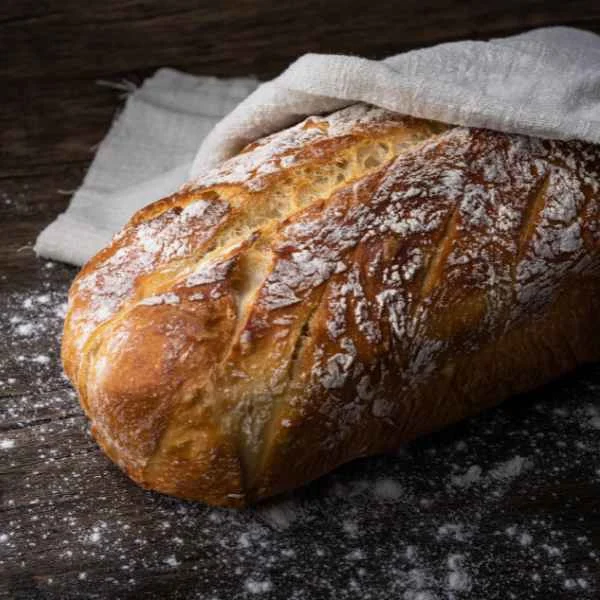 Crusty rustic loaf of fresh-baked bread dusted with flour on a dark board
