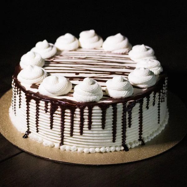 Round cake with white frosting, chocolate drizzle and whipped cream rosettes
