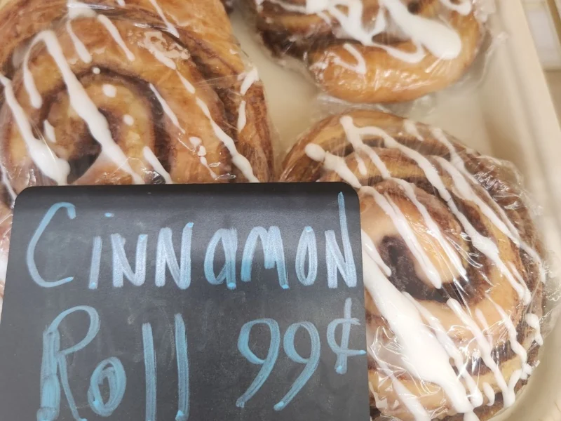 Iced cinnamon rolls behind a chalkboard sign reading Cinnamon Roll 99 cents