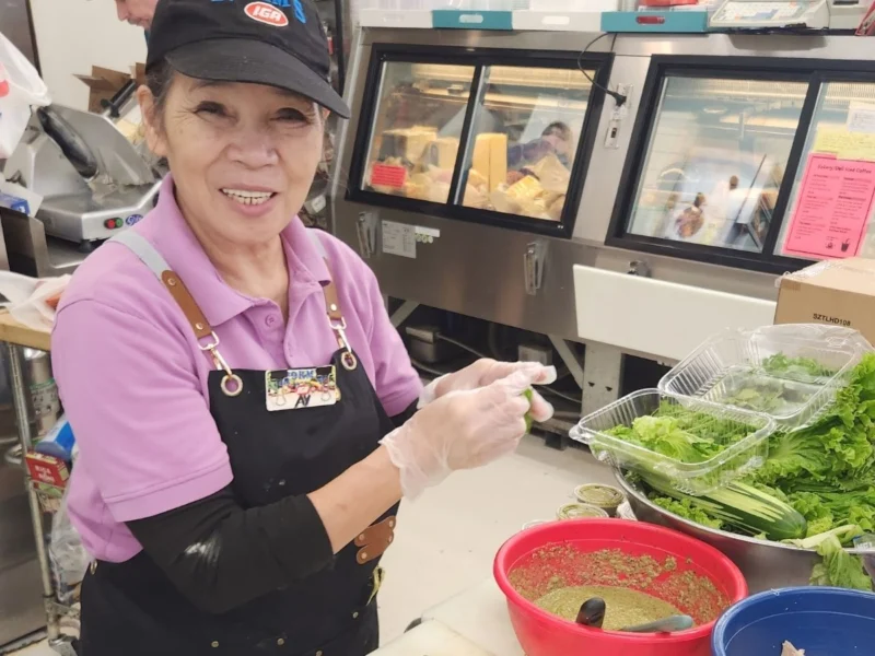 Chef Ay smiling while preparing fresh food in the deli
