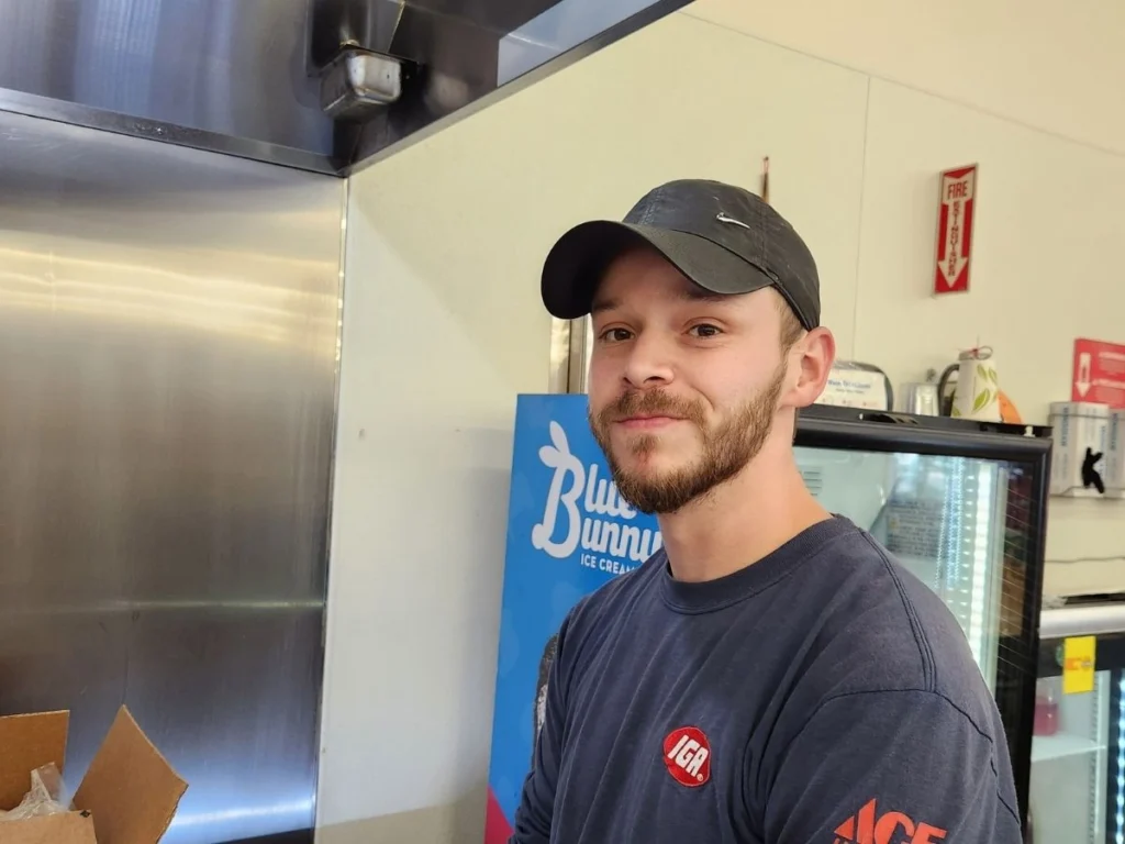 Smiling Olsens Marketplace employee in a cap and IGA shirt
