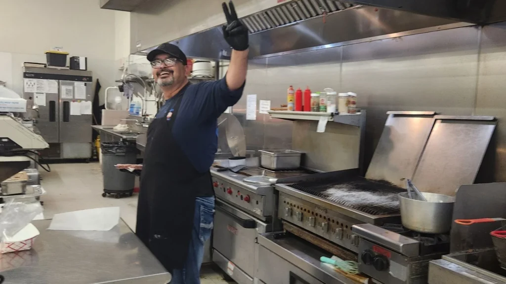 Olsens Patio Cafe cook waving from the flat-top grill