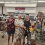 Three smiling shoppers with carts and their dogs inside Olsens Marketplace