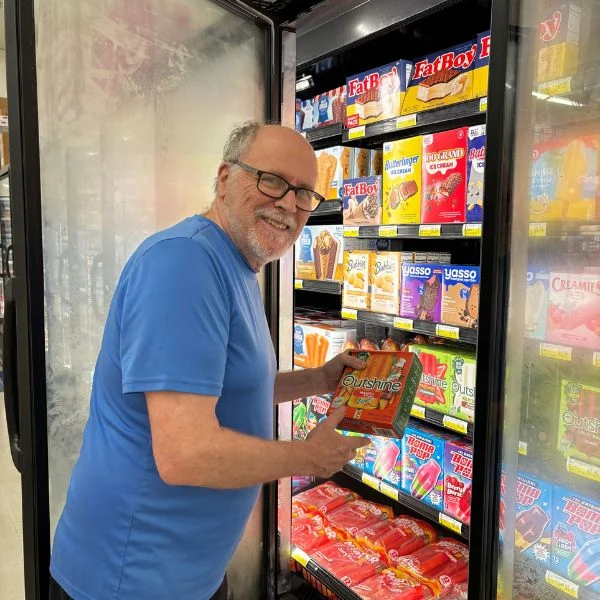 Smiling shopper choosing a frozen pizza from the freezer at Olsens Marketplace