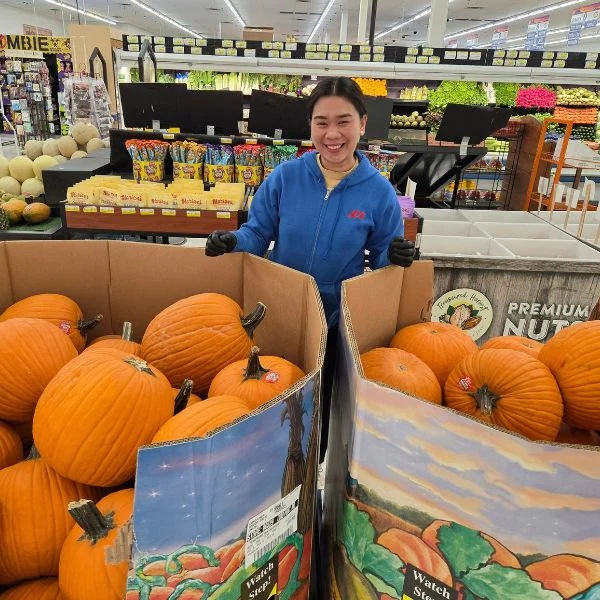 Smiling produce team member with fall pumpkins at Olsens Marketplace